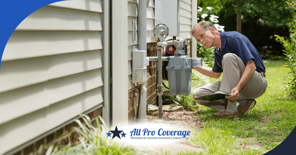 A man kneeling outside a home, closely inspecting the gas meter and surrounding utilities with a tablet in hand